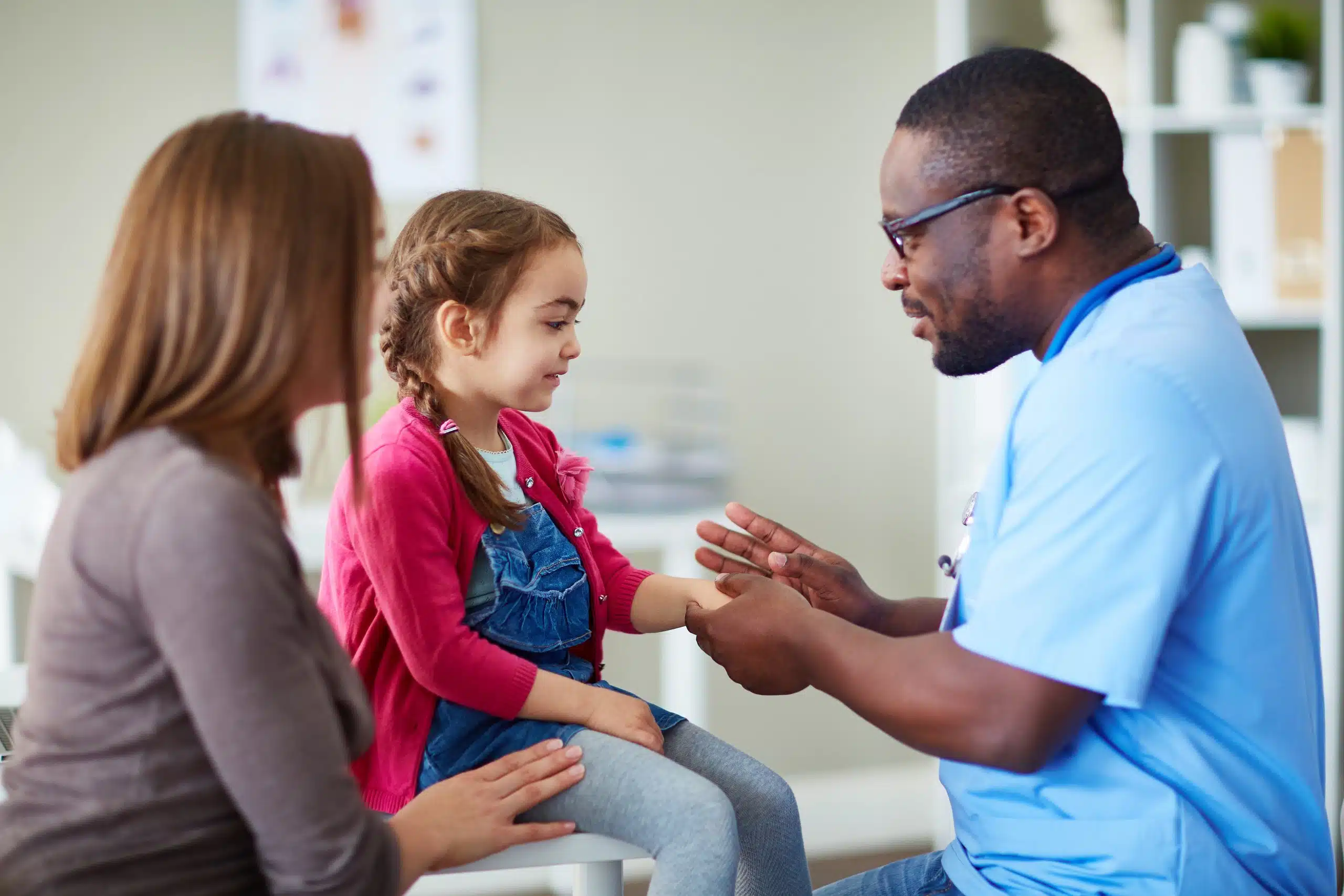 Visiting doctor Physician assistant helping a young girl with her mother sitting by.