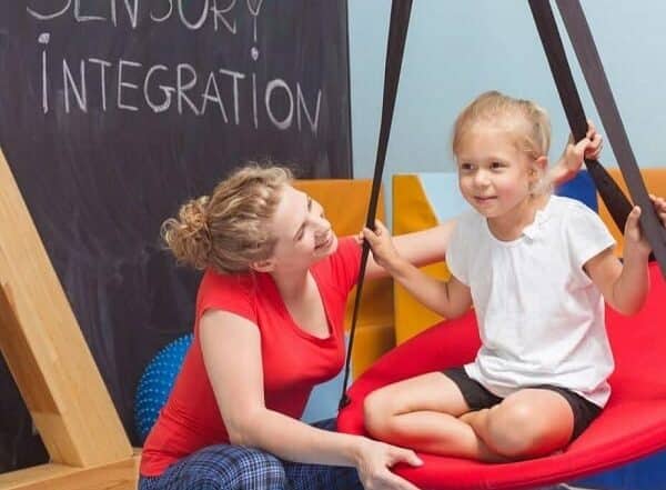 Woman helping a child play in a sensory integration space for therapy