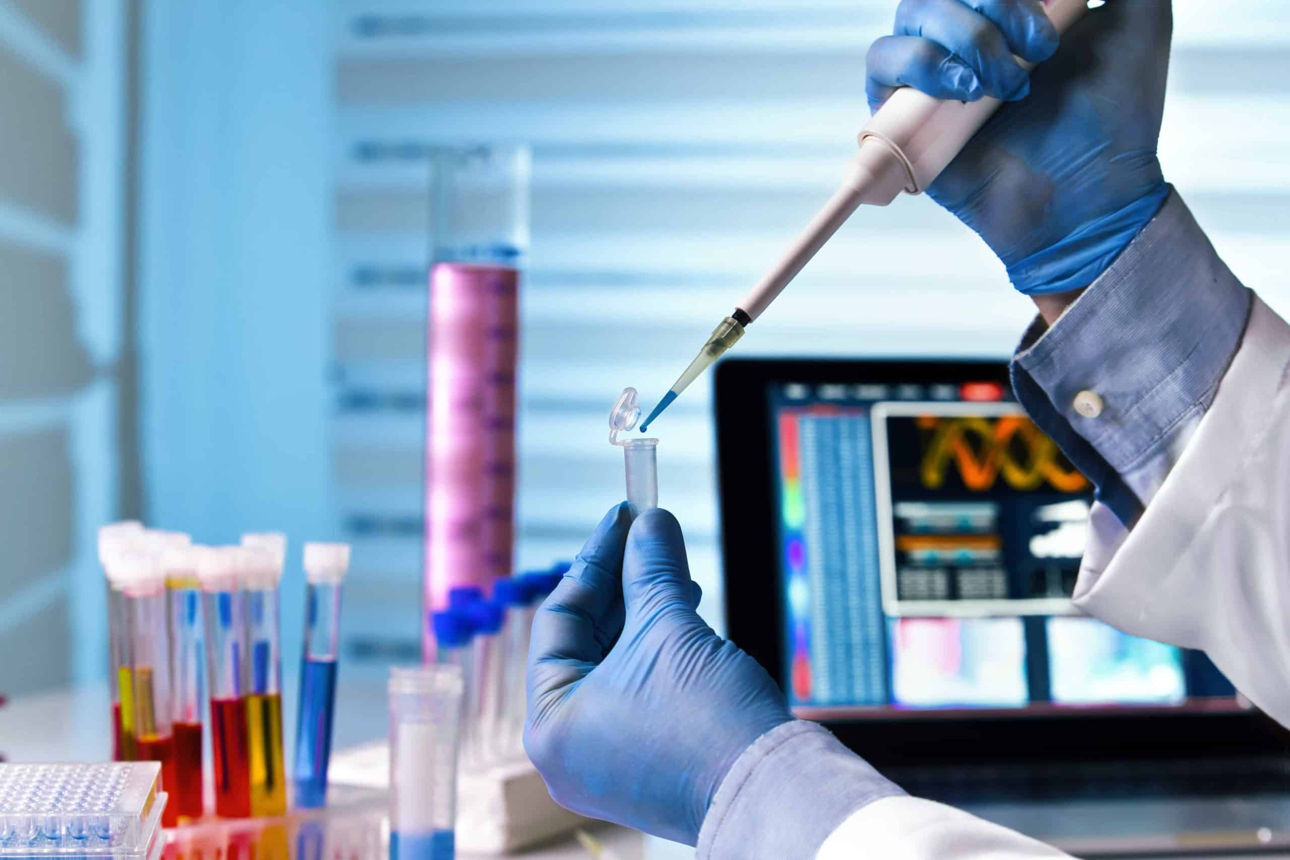 scientist holding tube and working with laptop at genetic lab / hands of engineer genetic working in laboratory