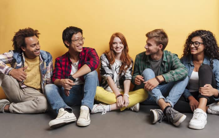 Multiethnic group of cheerful young friends talking and laughing over yellow background