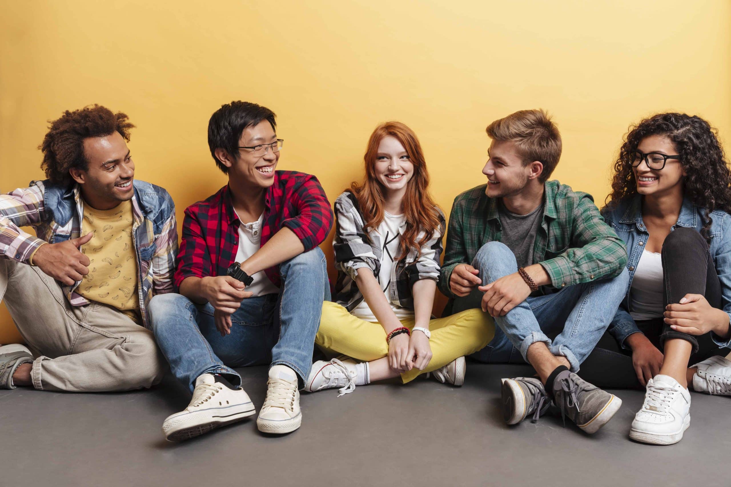 Multiethnic group of cheerful young friends talking and laughing over yellow background