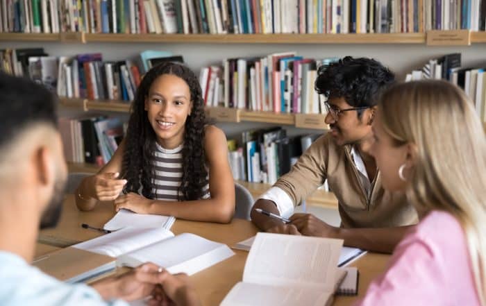 Group of multinational high school or university students engaged in exam preparation, sharing ideas, testing each other, studying together met in library, focus on African girl explain point of view