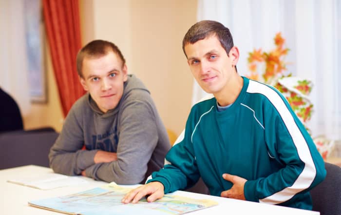cheerful adult men with disability sitting at the desk in rehabilitation center