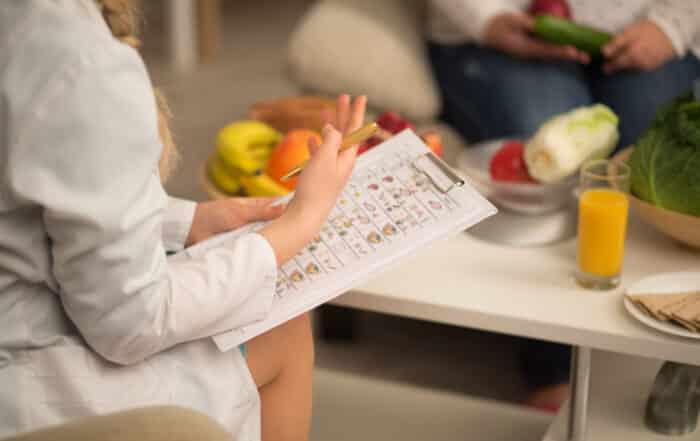 Close up image of dietitian in white gown. holding die plan for patient, having fruits and vegetables on the white table