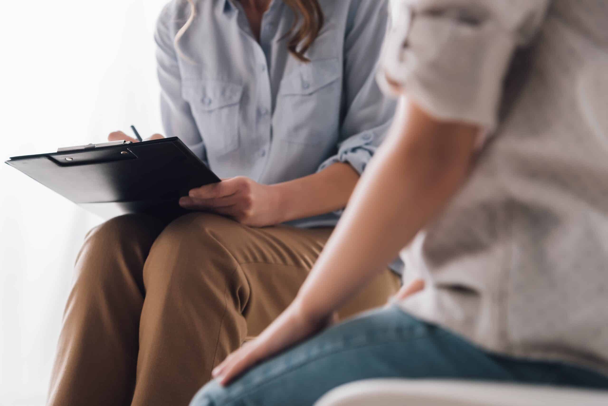 Cropped shot of psychologist with clipboard sitting in front of child