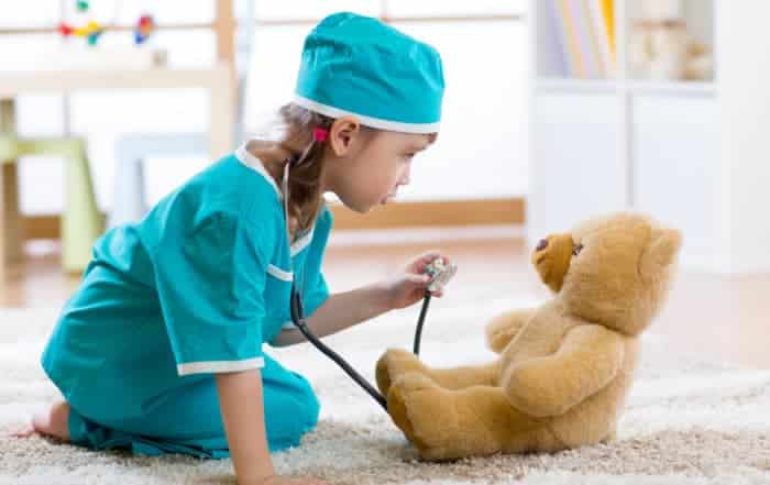 Funny child girl playing with teddy bear and pretending she is a doctor in hospital