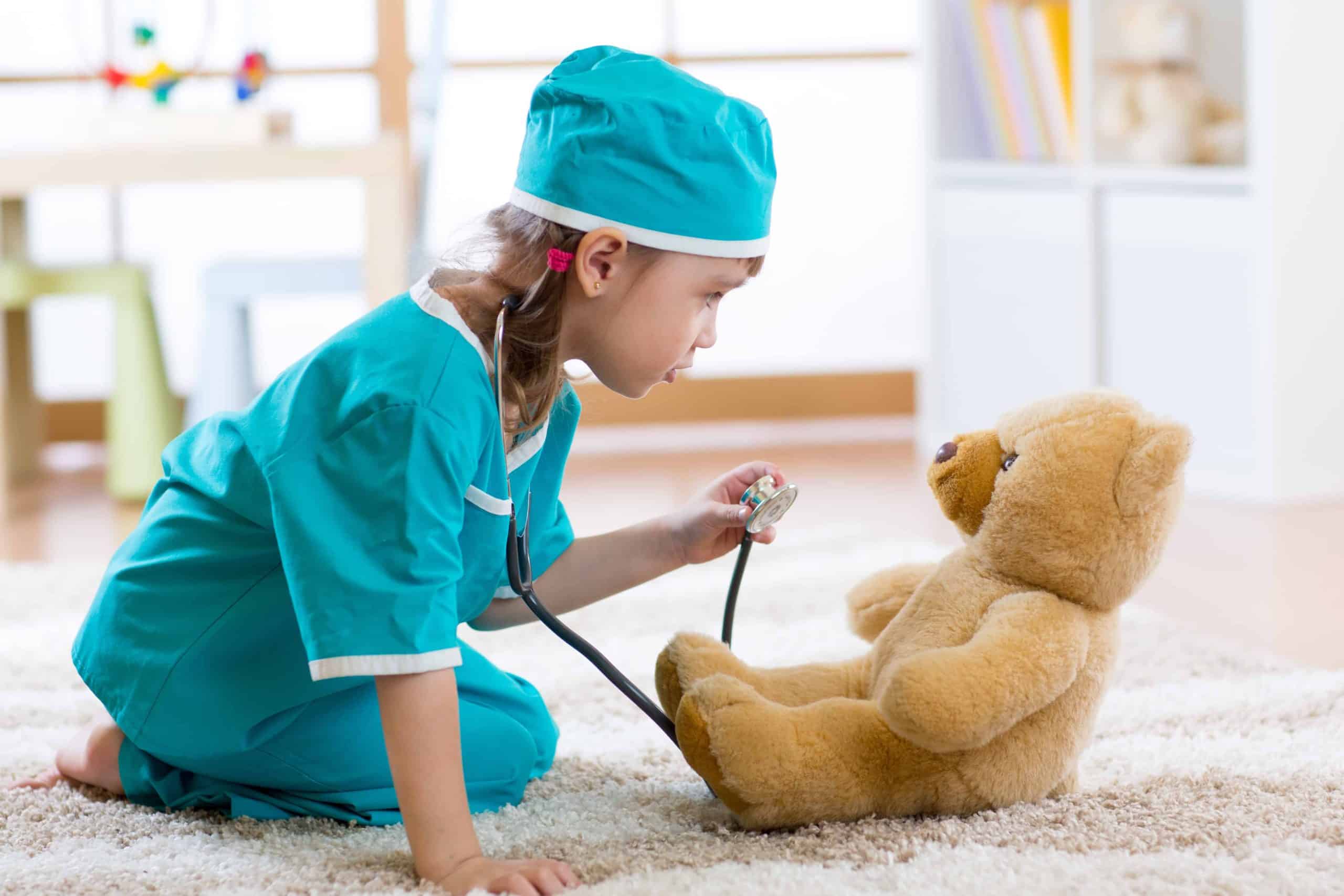 Funny child girl playing with teddy bear and pretending she is a doctor in hospital
