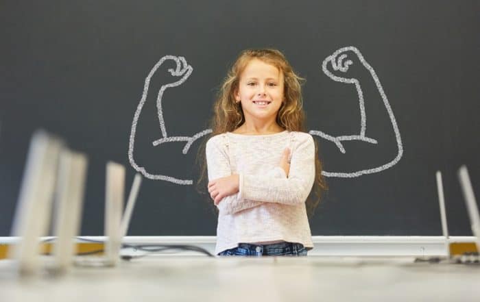 Child standing proudly in front of a board with bold shoulder drawings, symbolizing strength