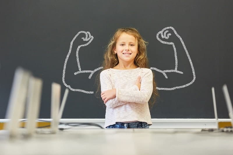 Child standing proudly in front of a board with bold shoulder drawings, symbolizing strength