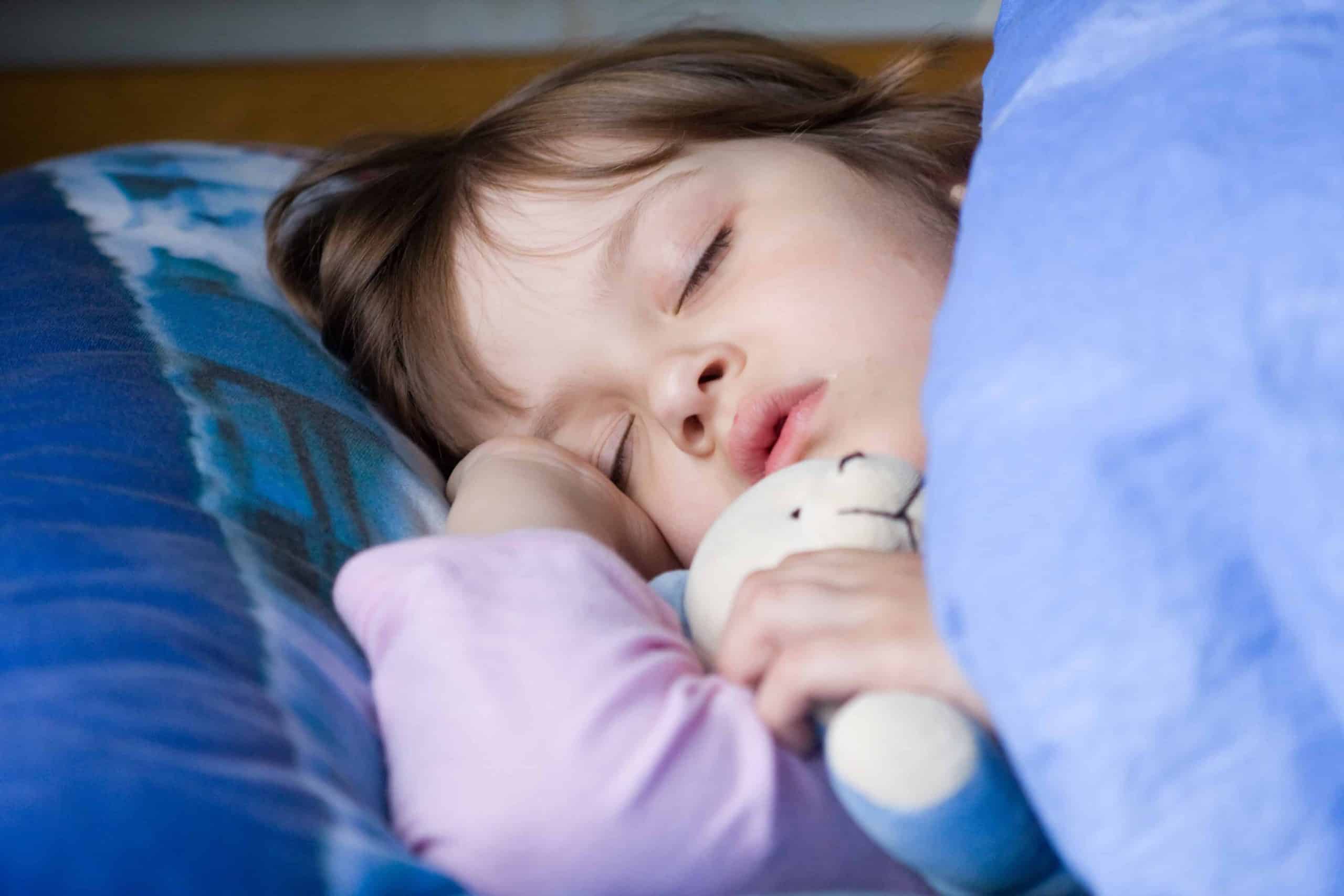 kid is sleeping on the bed with tedy bear