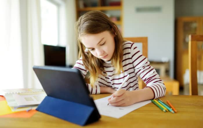 Preteen schoolgirl doing her homework with digital tablet at home. Child using gadgets to study. Education and distance learning for kids. Homeschooling during quarantine. Stay at home entertainment.