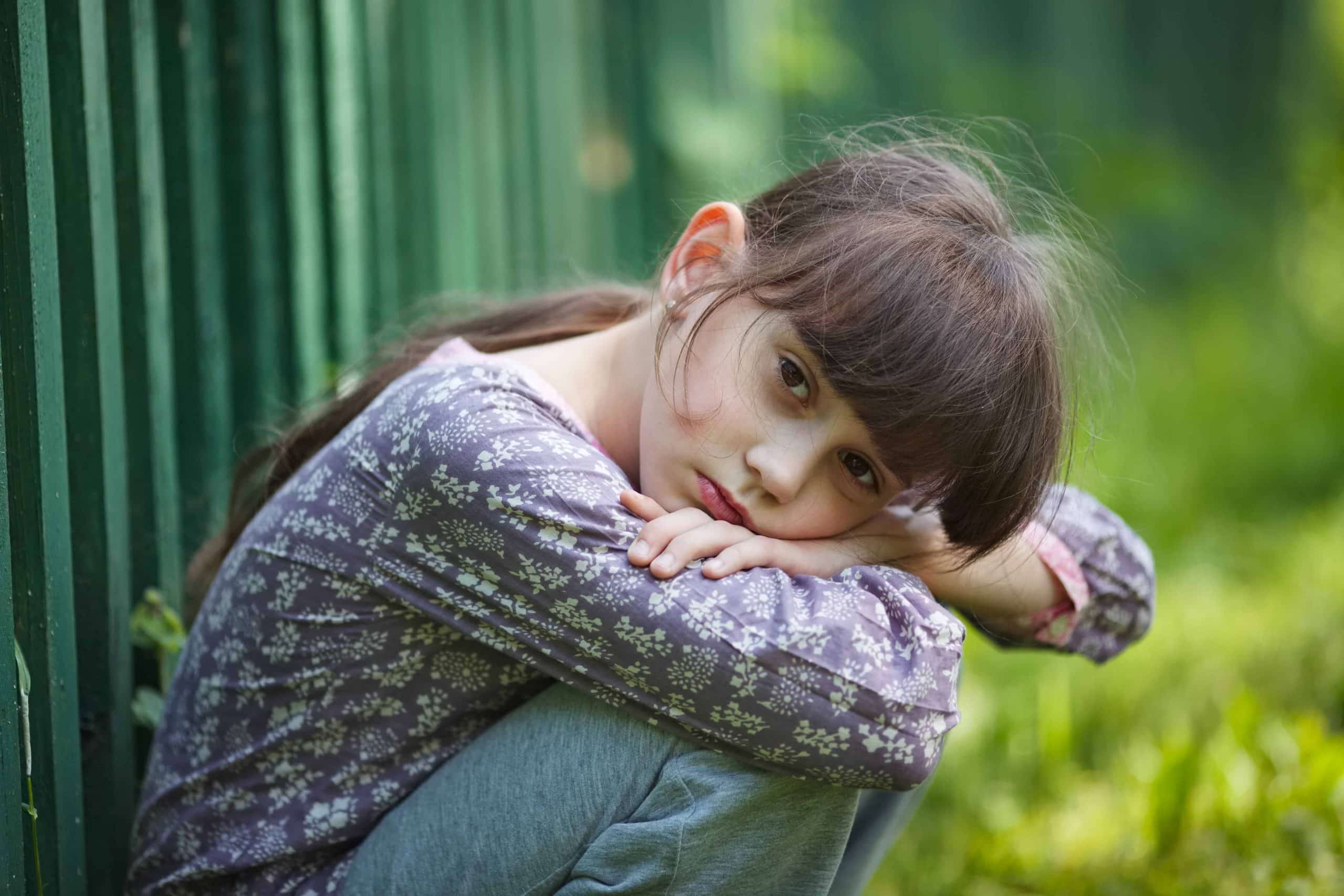 Lonely child with a sad expression in the yard