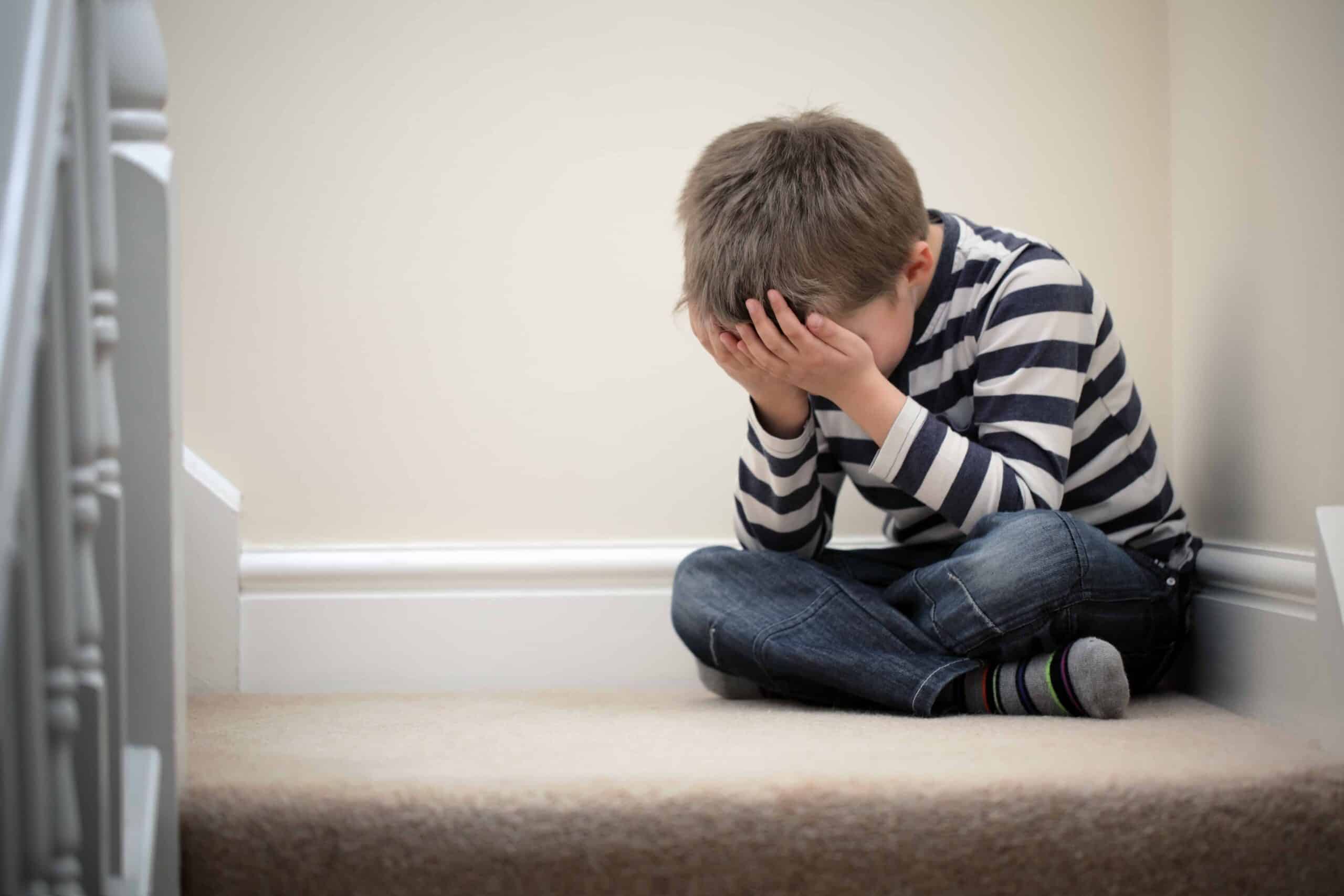 Upset child with head in hands sitting on staircase