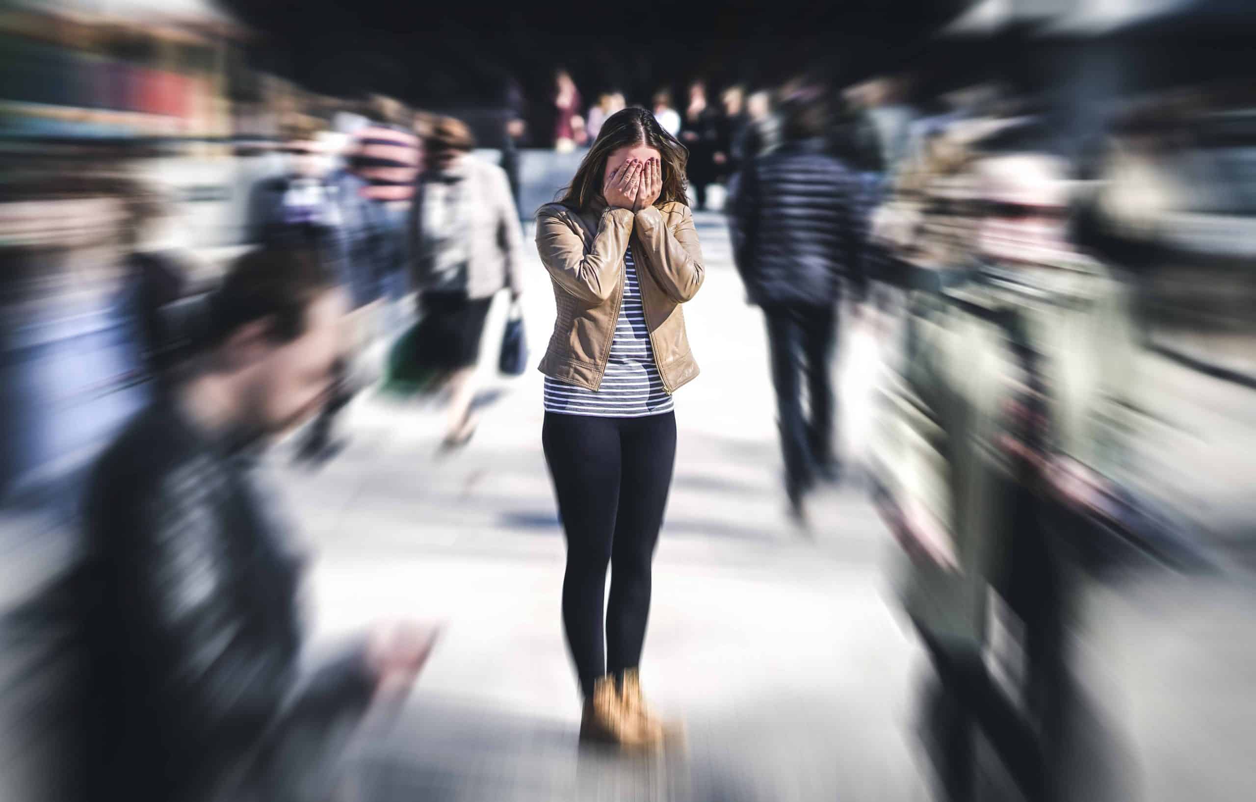woman having panic disorder in city. Psychology, solitude, fear or mental health problems concept. Depressed sad person surrounded by people walking in busy street.