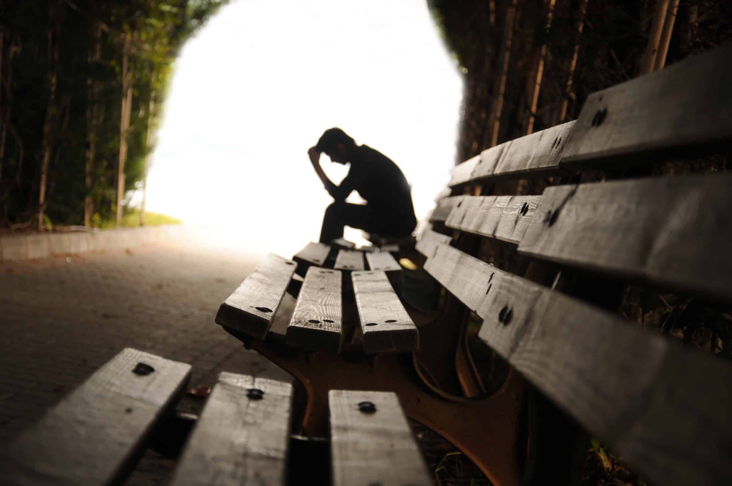 Man struggling with depression, sitting quietly on a street bench