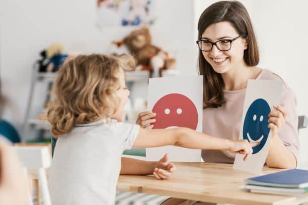 Woman works with a child to identify happy and sad feelings using cards