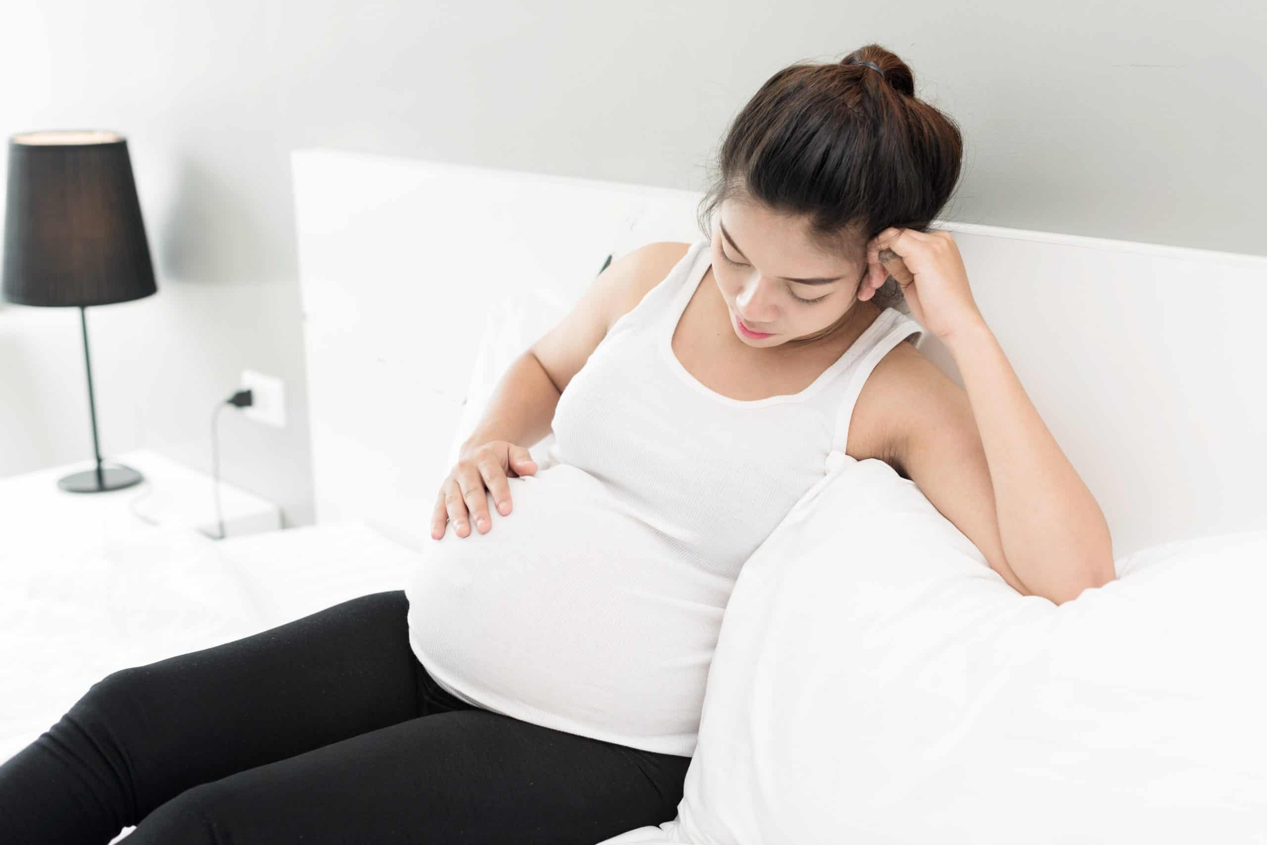 Pregnant woman is sitting on the white bed