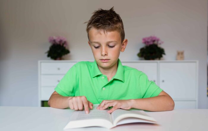 Young boy in green polo shirt having challenges reading a text in a school book.