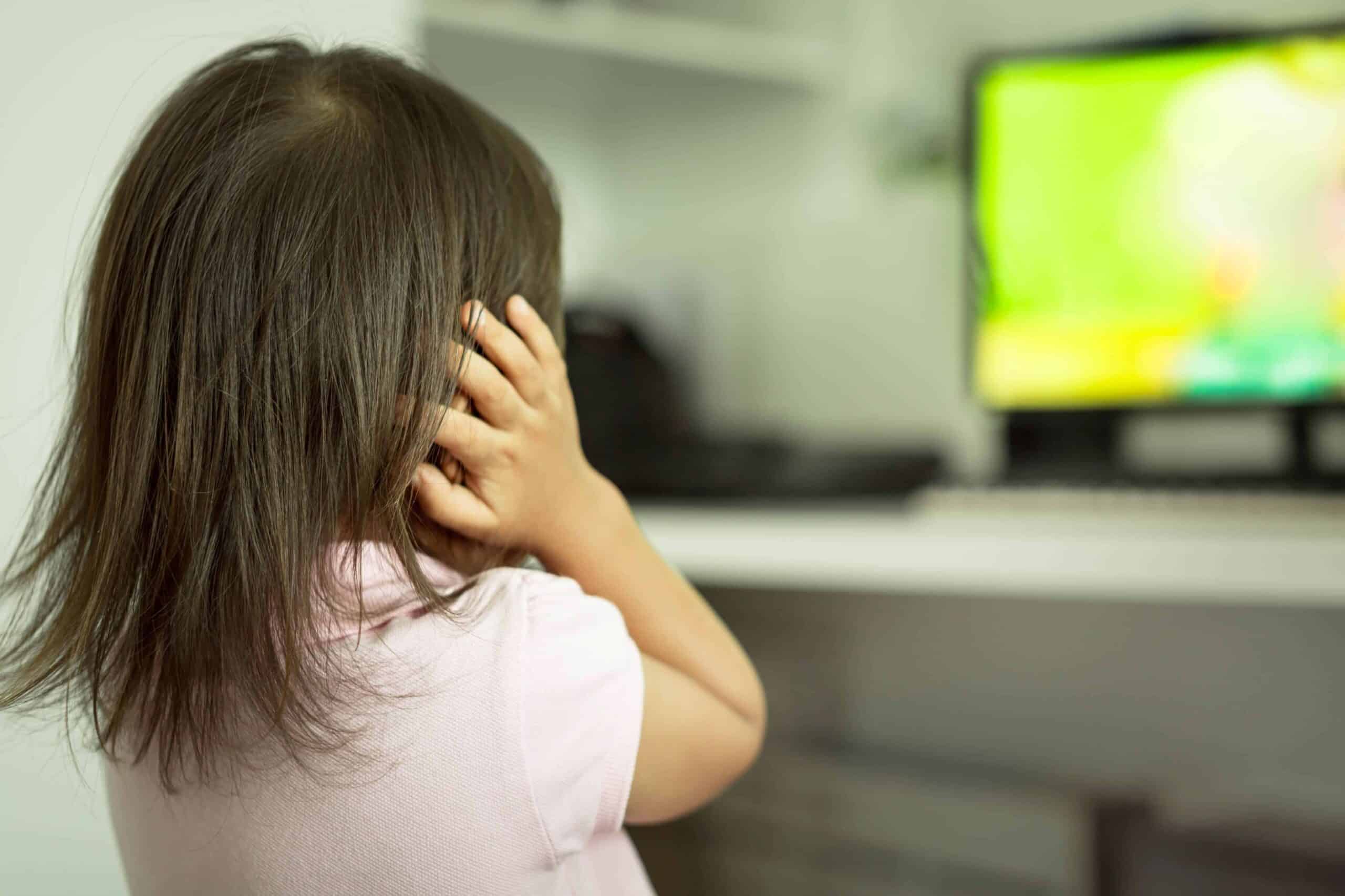 sensory pain sm Child covering her ears while looking at a TV screen in the background