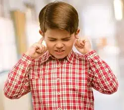 Toddler child with green eyes covering ears ignoring annoying loud noise, plugs ears to avoid hearing sound. Noisy music is a problem. at school corridor