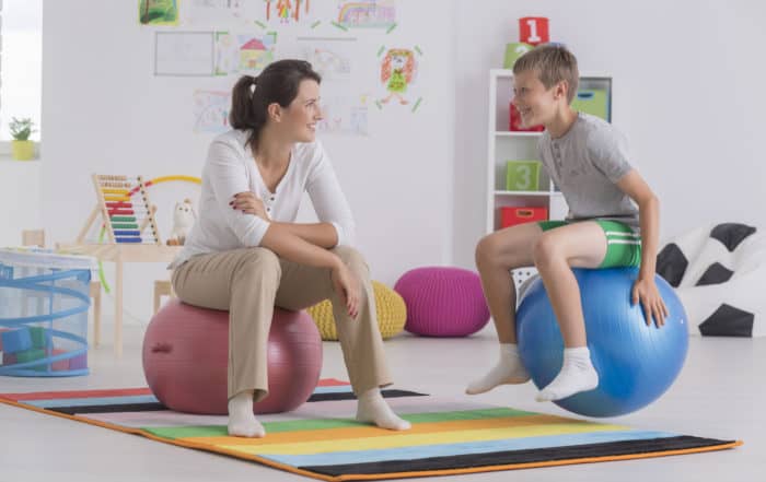 Physiotherapist and happy boy sitting on gym ball