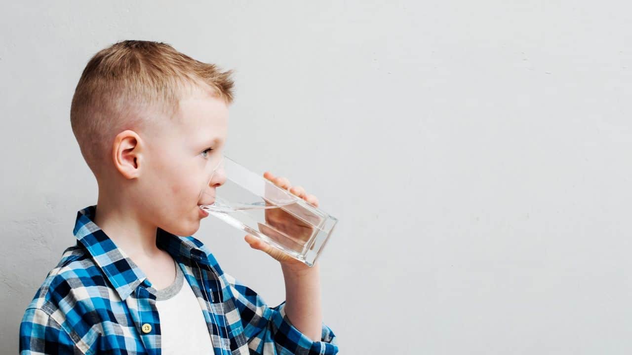 Young kid sipping water from a clear glass