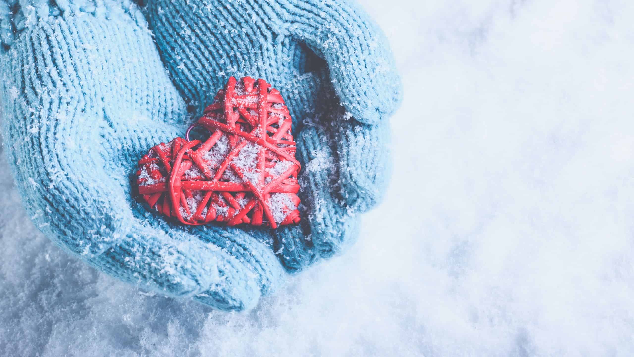 Woman wearing blue gloves holding a red heart-shaped Christmas ornament