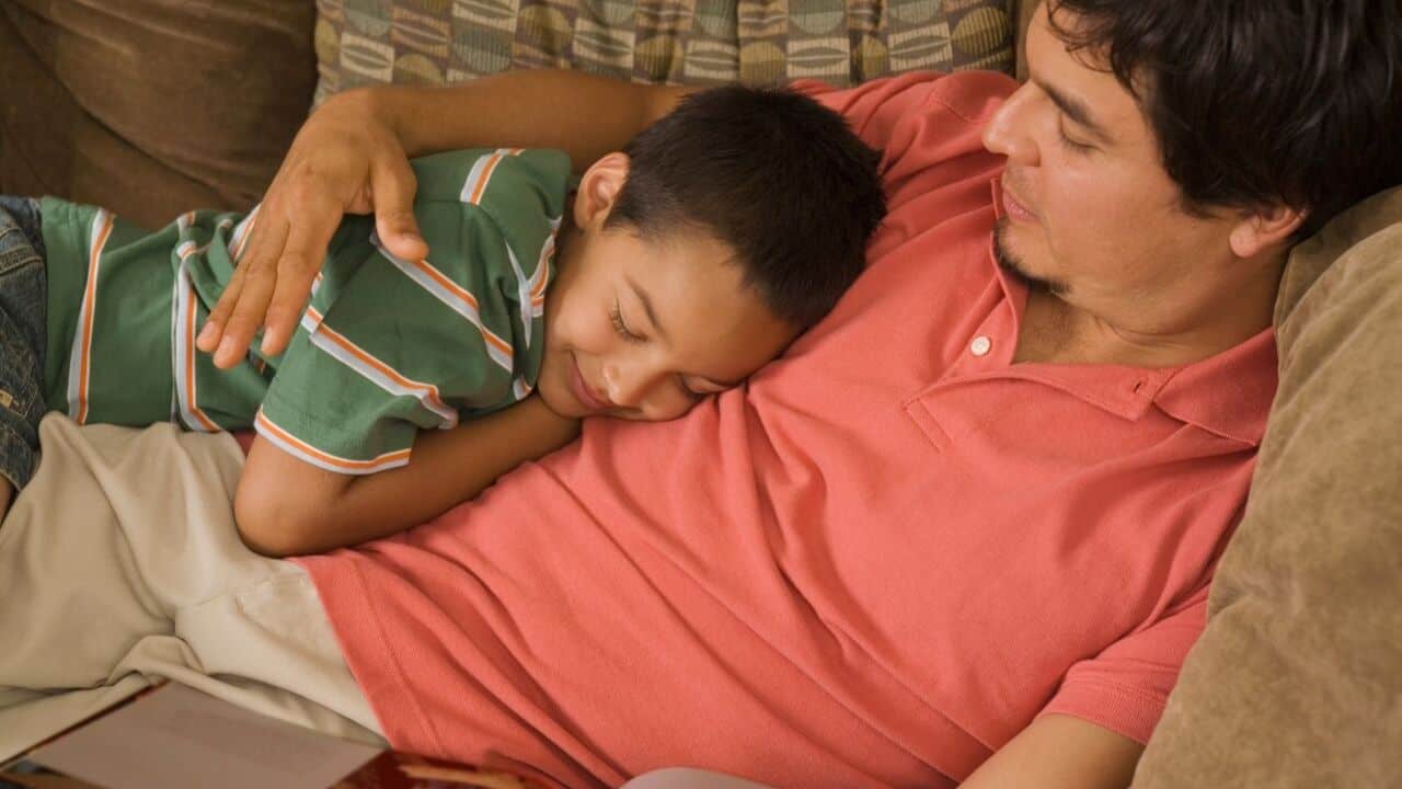 Kid napping while hugging his father, showing love and comfort.