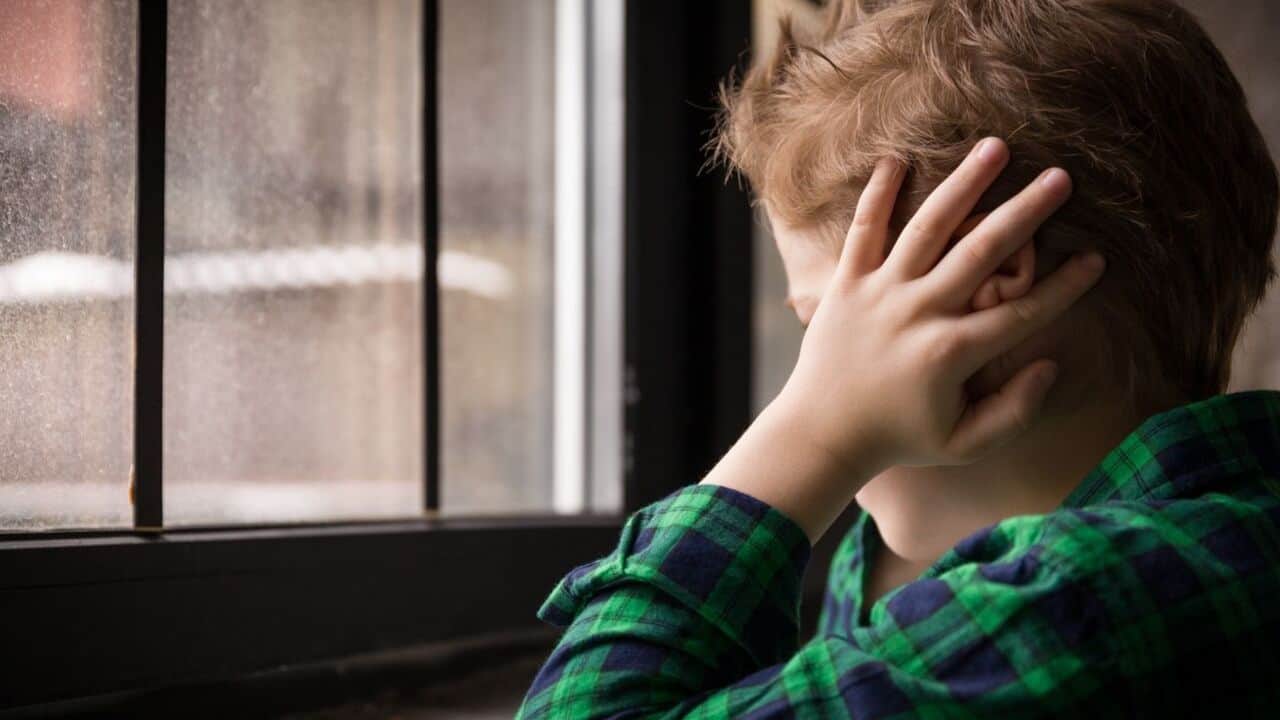 Young boy covering his ears and looking outside through the window