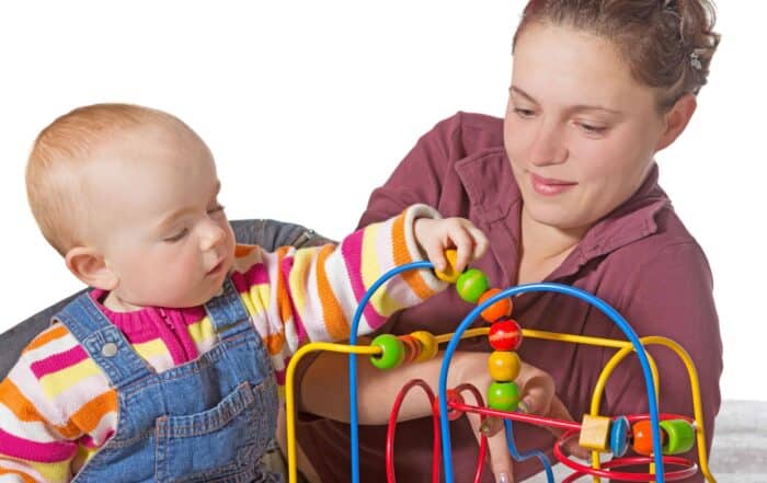 Baby with development delay being stimulated to develop muscle coordination and movement on a bead maze watched by an adult woman