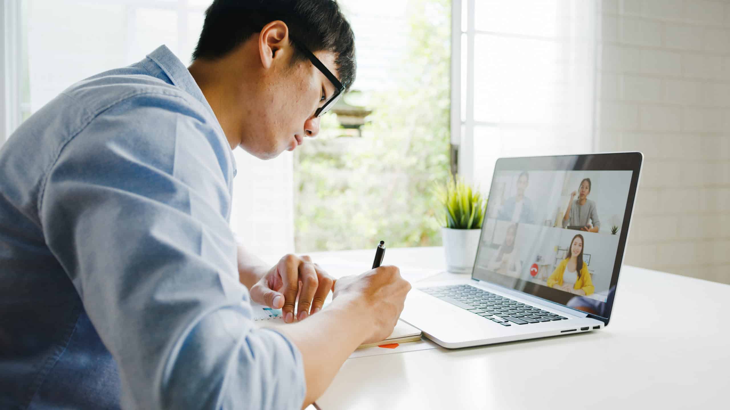 Man on a video call, writing notes in a notebook during the session